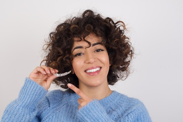 Smile with Invislaign: Patient holding a set of clear aligners in Arlington during their visit to an Invisalign orthodontist at a trusted provider of Invisalign clear aligners, learning how clear aligners can treat misaligned teeth.